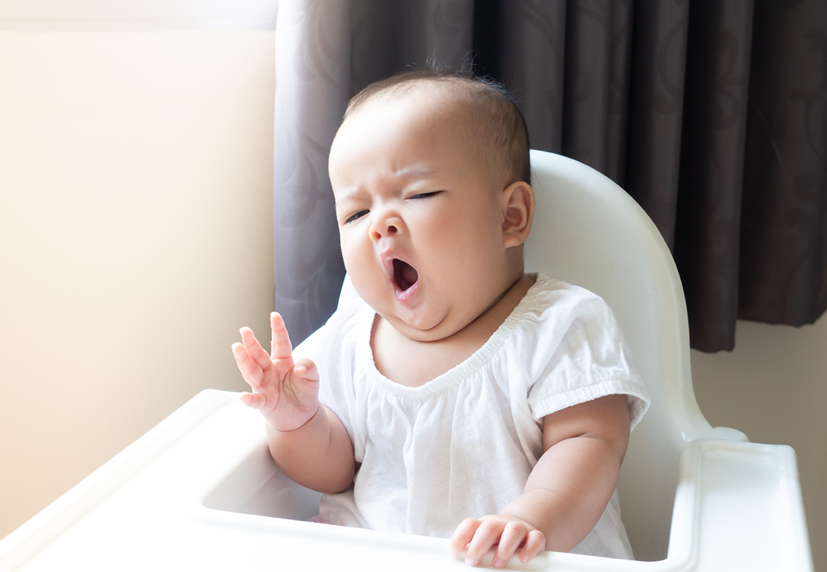 Asian,Baby,Girl,Sitting,And,Yawning,On,White,High,Chair